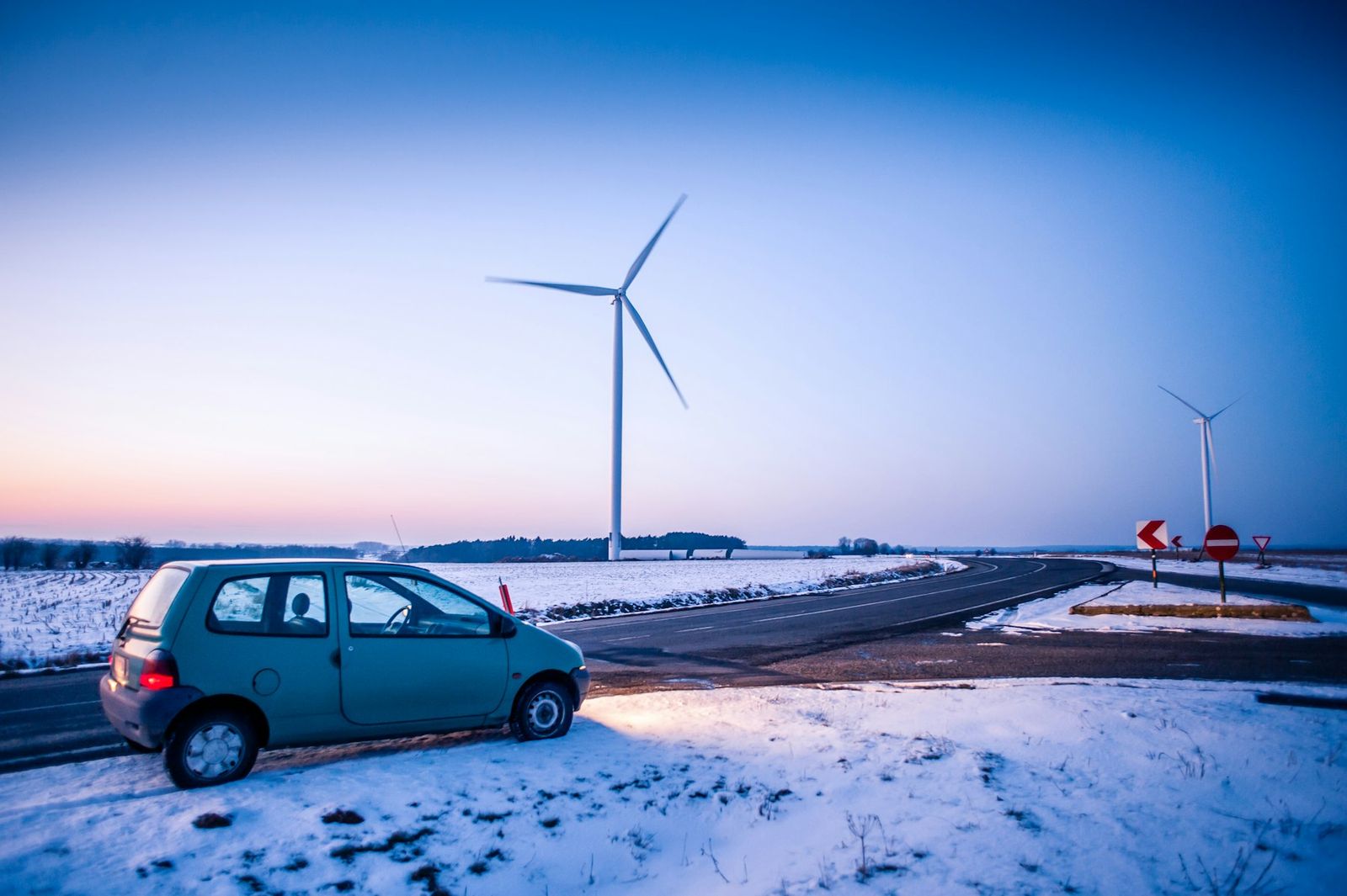 Renault Twingo bleue garée dans la neige près d'éoliennes